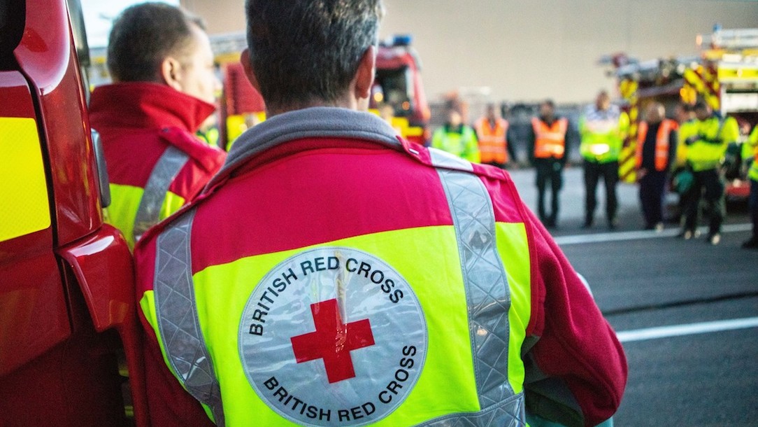 A British Red Cross volunteer standing with other emergency services. Gwirfoddolwr y Groes Goch Brydeinig yn sefyll gyda gwasanaethau brys eraill. 