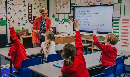 School children raising their hands to answer a teacher's question